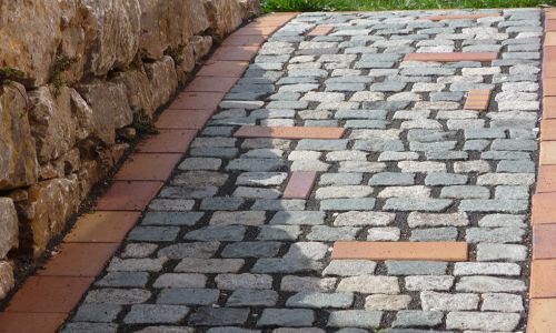Gartenweg aus Natursteinpflaster mit Ziegelrand und Natursteinmauer