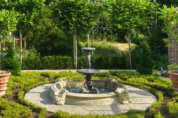 Elegante Gartengestaltung mit Natursteinbrunnen, Kiesflächen und strukturierter Bepflanzung