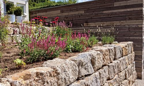 Gartengestaltung mit Natursteinmauer, Staudenbeet und Holzsichtschutz